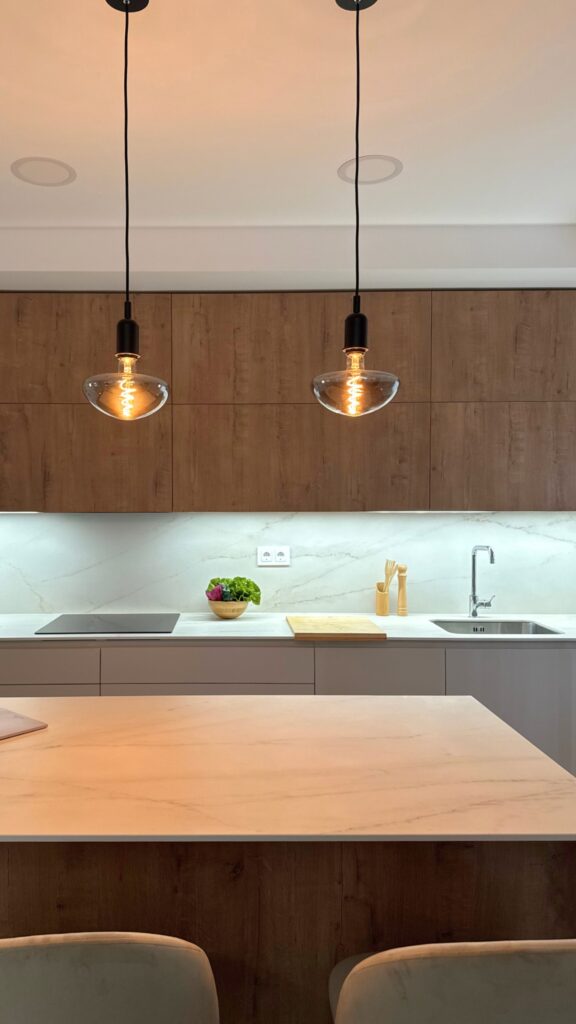 Cocina con isla central en madera y blanco con luces colgantes y electrodomésticos integrados