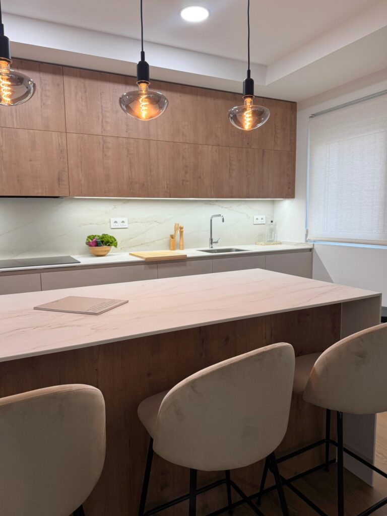 Cocina con isla central en madera y blanco con luces colgantes y electrodomésticos integrados