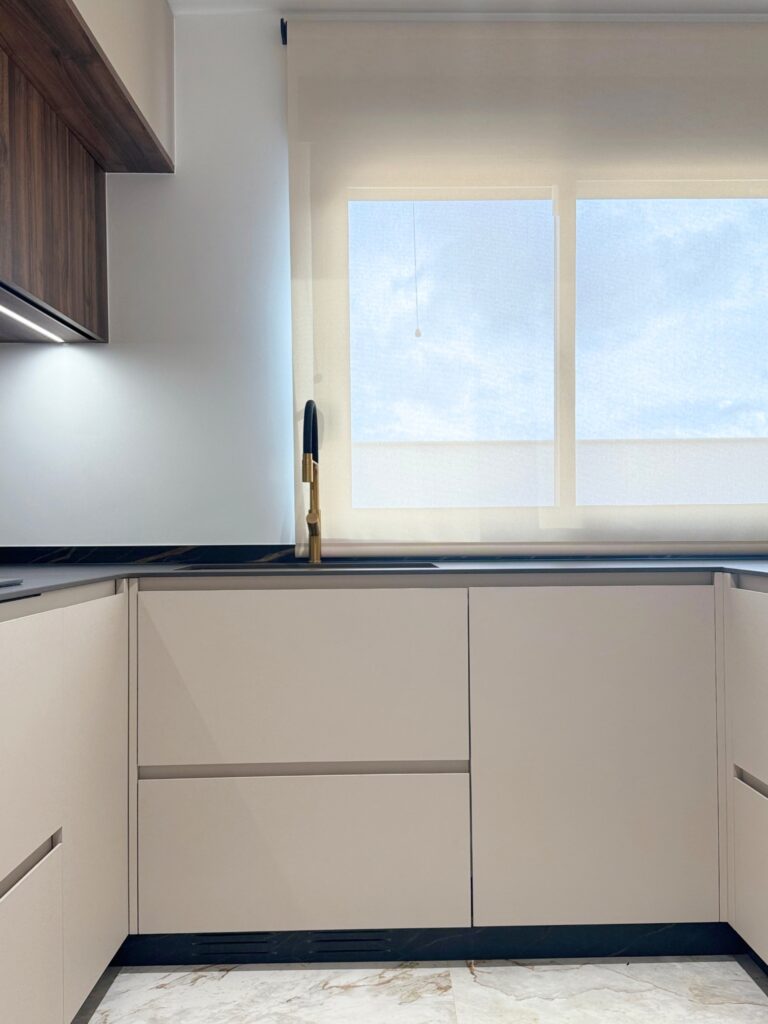 Cocina de diseño con isla central en mármol negro, muebles en beige mate y colgantes dorados