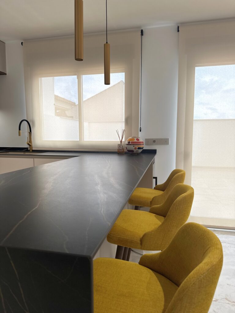 Vista general de cocina moderna con isla en negro, taburetes mostaza y luz natural